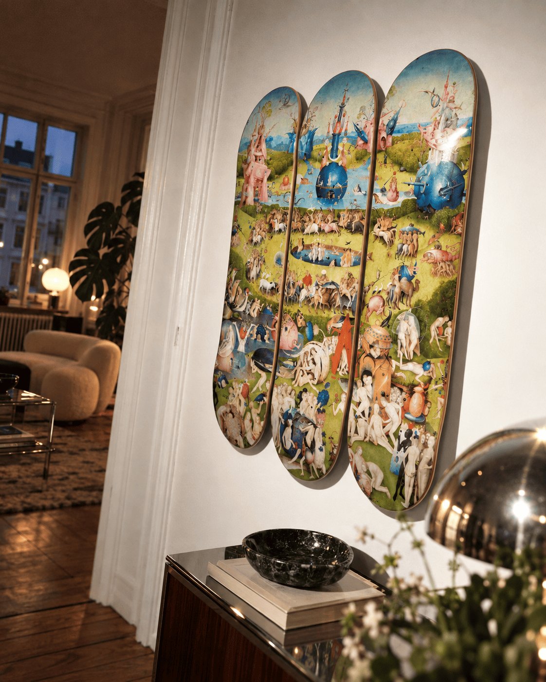 Garden of Earthly Delights skateboard triptych above a sideboard in warm evening light