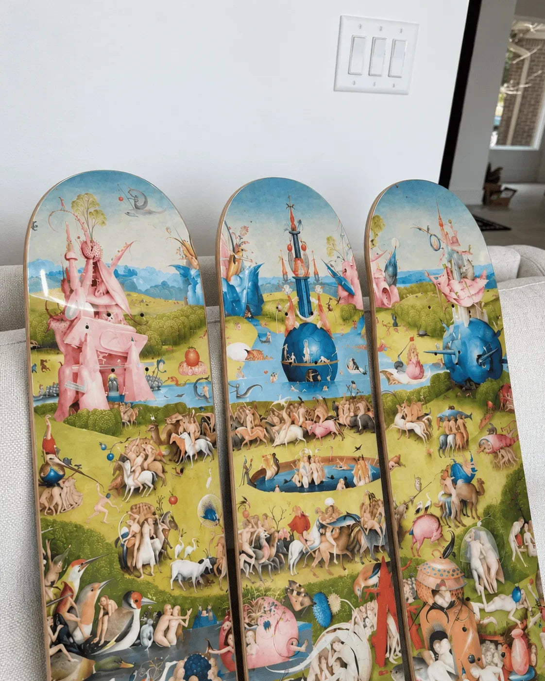 Bosch Garden of Earthly Delights triptych printed on three maple skateboard decks, leaning against a sofa