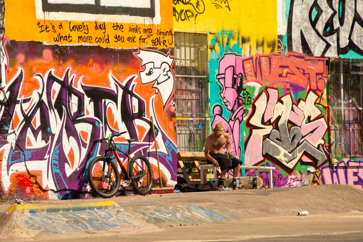 Man sits by bikes against colorful graffiti wall.