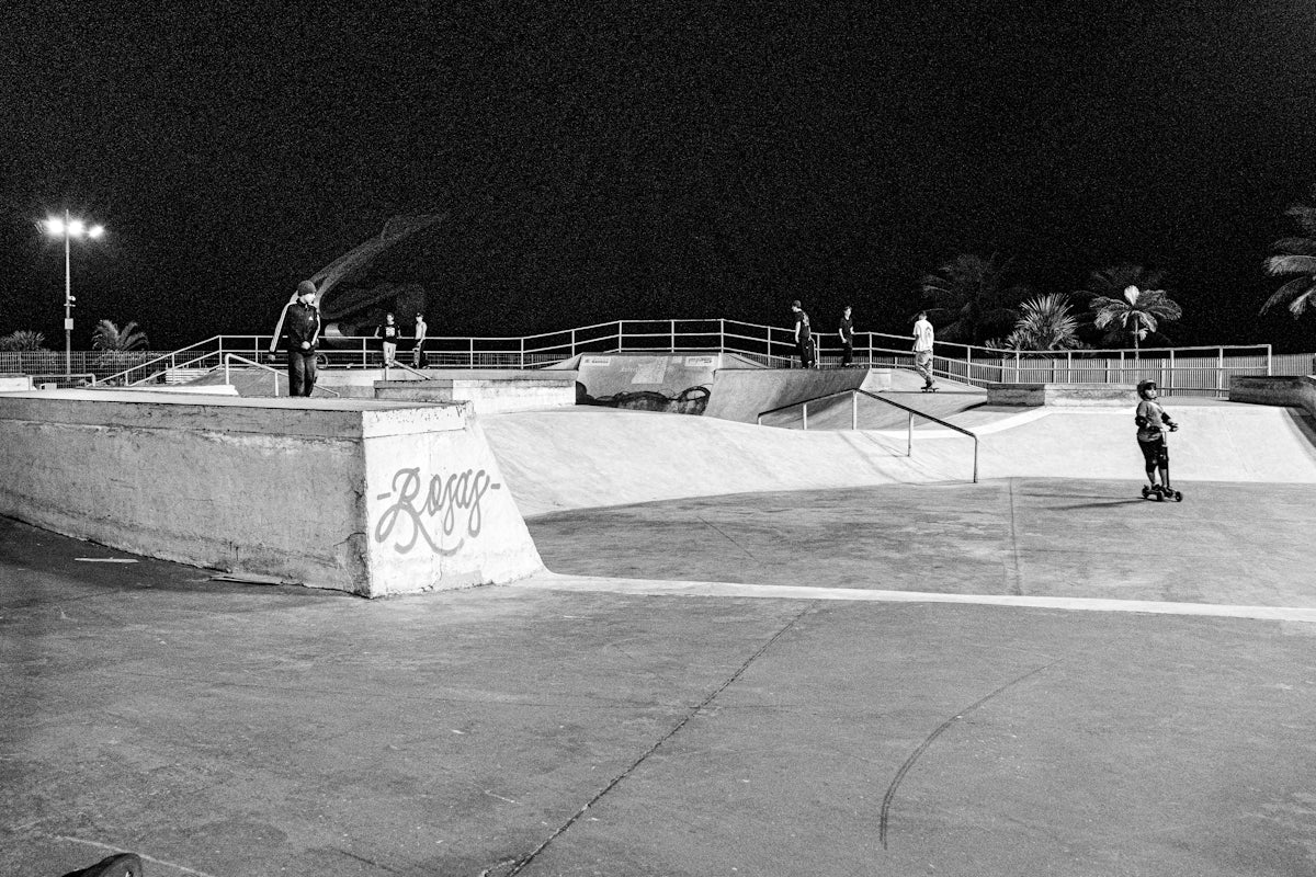 People skateboarding in a concrete park at night